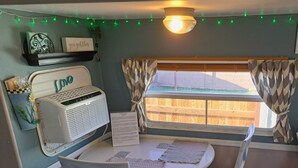Una habitación de estilo vintage con una mesa redonda, dos sillas, una máquina de escribir antigua y un ventanal con cortinas.