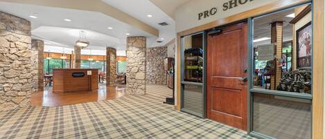 A hotel lobby with a check-in counter, a pro shop, and a staircase leading to another level.