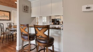 Una cocina moderna con armarios blancos, un termostato digital y un comedor con sillas y una mesa de madera.