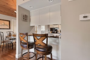 Una cocina moderna con armarios blancos, un termostato digital y un comedor con sillas y una mesa de madera.