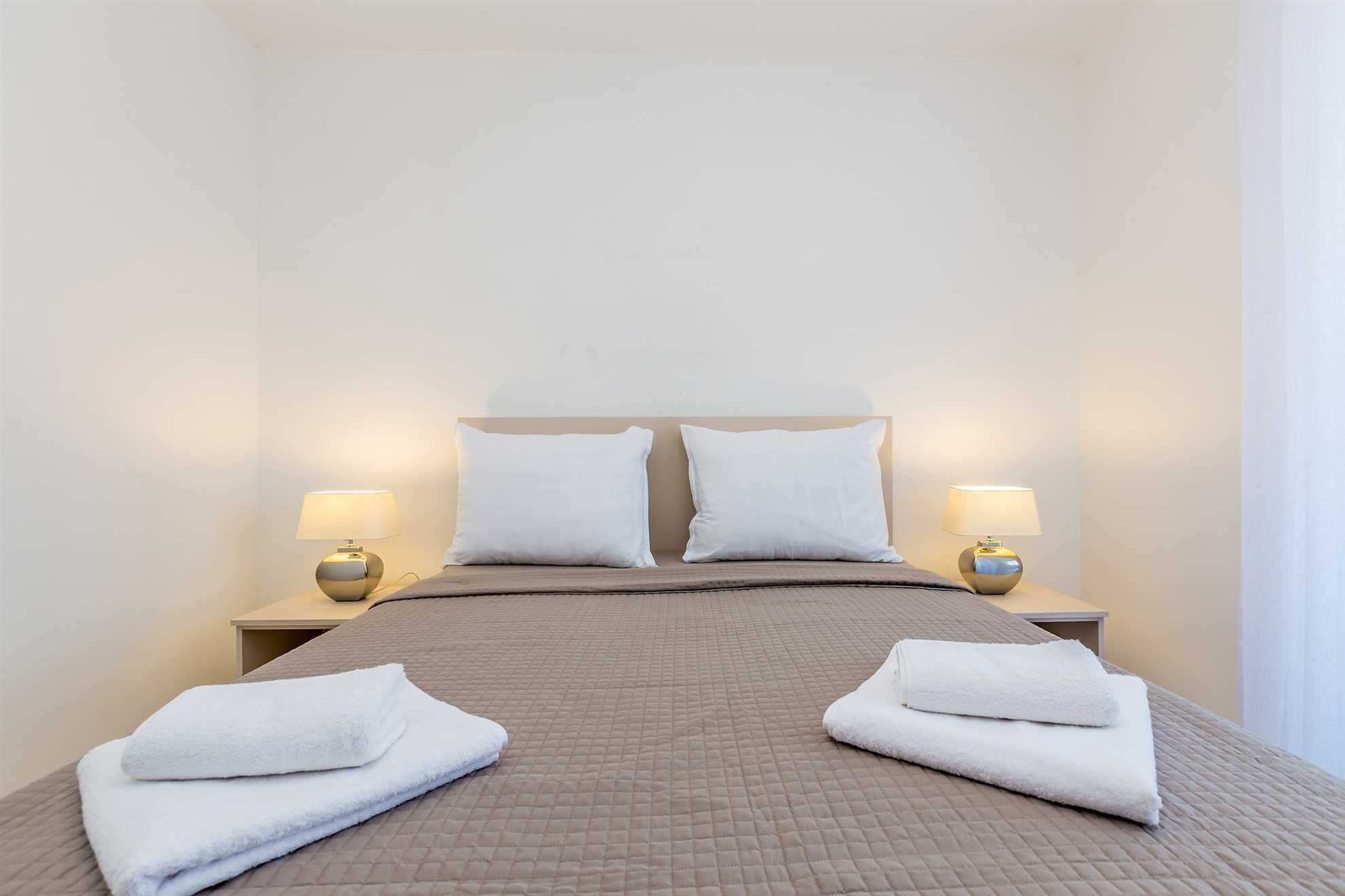 A neatly made bed with a quilted headboard, two white pillows, and two bedside lamps.