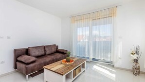 A modern living room with a brown leather sofa, a wooden coffee table with fruit, and a large window with sheer curtains. - Apartment LAGANINI III (Njivice)