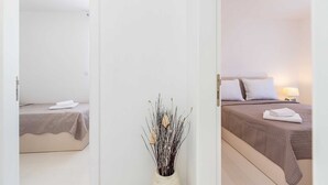 A hotel room with a bed, a bedside table with a lamp, and a vase with dried plants. - Apartment LAGANINI III (Njivice)
