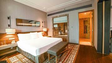 A hotel room with a large bed, bedside tables, a bench, a mirror, and a shower area.