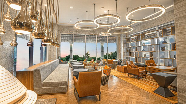 Un área de descanso moderna con diversas opciones de asientos, incluyendo sofás y sillones, y una amplia estantería llena de objetos decorativos.