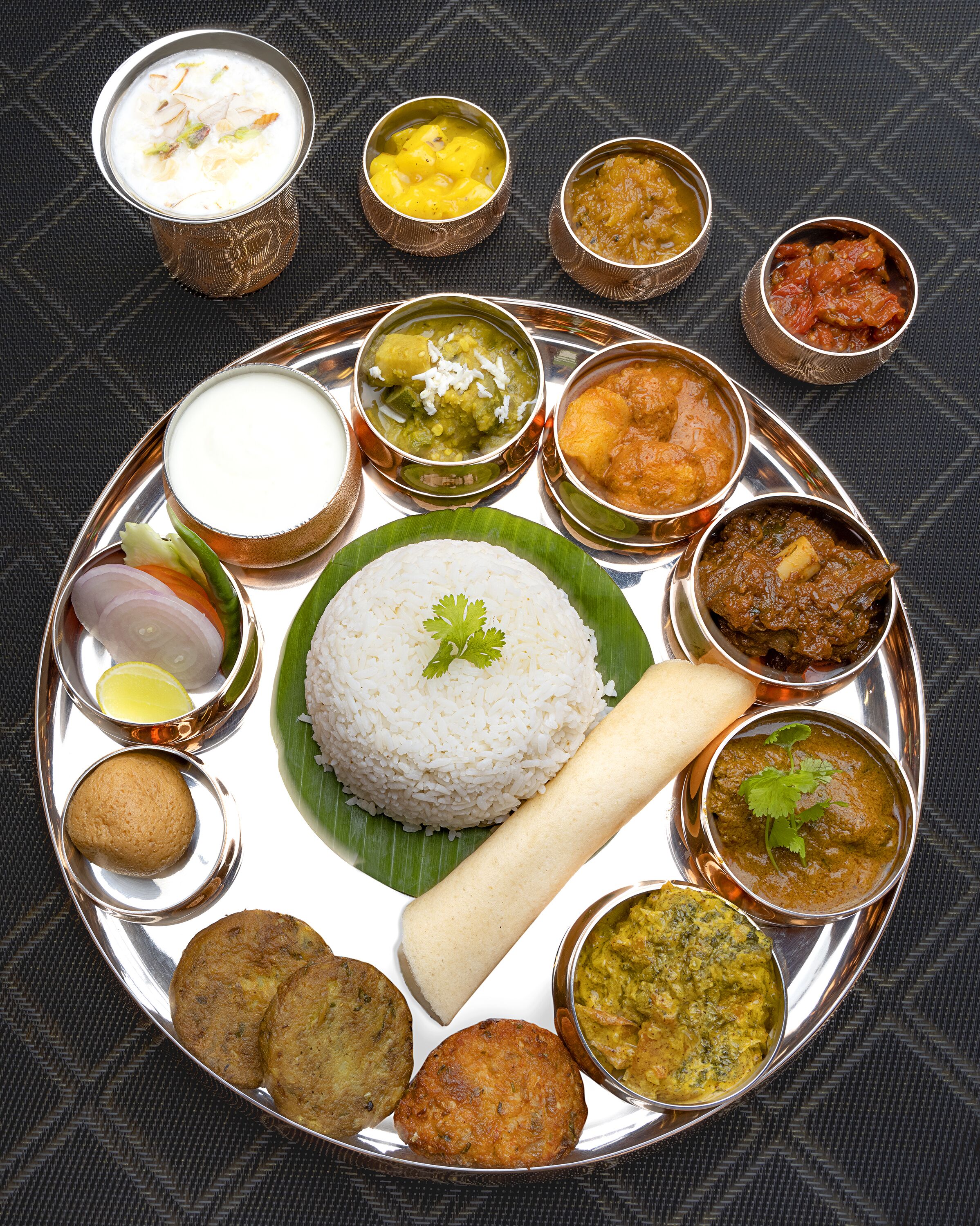 Un pasto tradizionale del Sud dell'India con riso, curry e diverse pietanze servite su un vassoio di metallo.