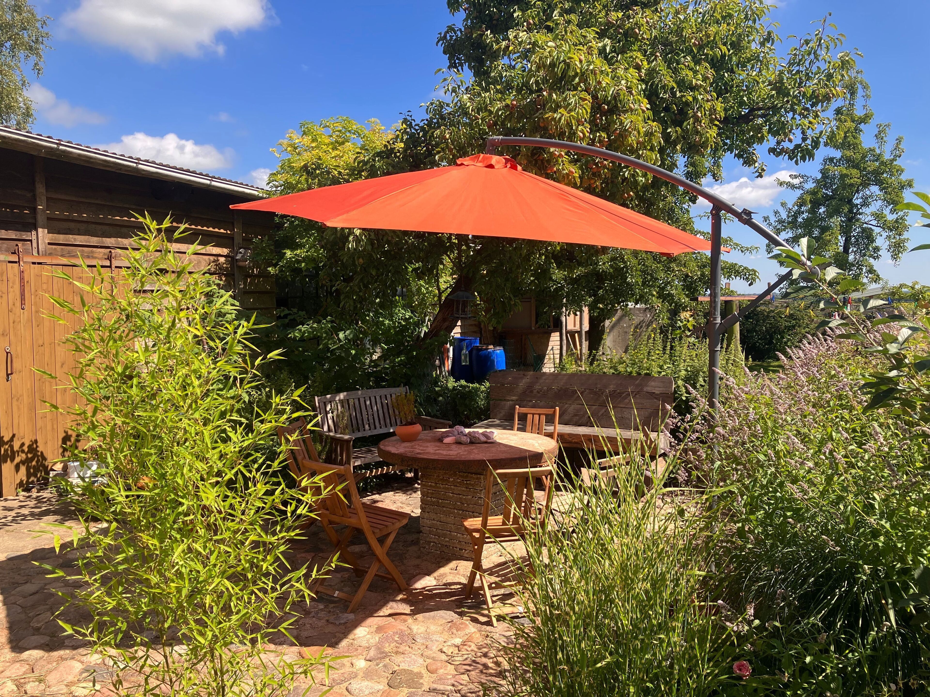 Une terrasse avec une table et des chaises, une clôture en bois et un parasol rouge.
