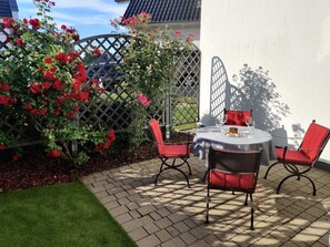 A patio with a table and chairs, surrounded by a lattice fence and blooming red roses.