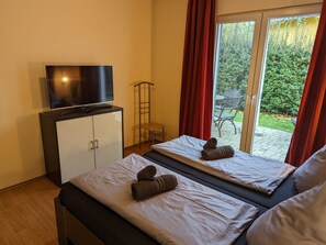 A hotel room with two beds, a TV on a cabinet, and a sliding glass door to the outside.