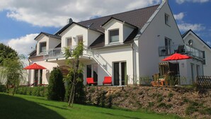 Ein zweistöckiges Haus mit Balkon, einem roten Regenschirm und einem kleinen Garten.