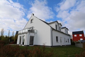 A modern two-story house with a balcony, large windows, and a well-maintained lawn.