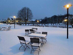 A snow-covered outdoor seating area with tables and benches, street lamps, and buildings in the background. - Sweet spot at Fleesensee (Göhren-Lebbin)