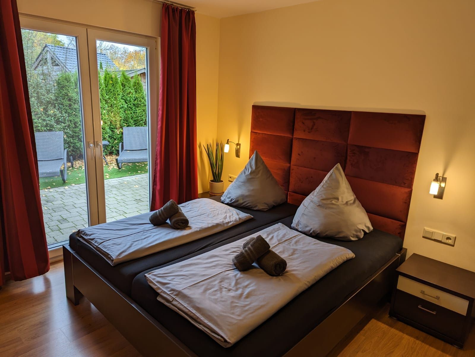 Ein Doppelbett mit zwei Kissen, ein Nachttisch und eine Topfpflanze.