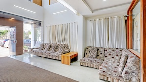 A modern lobby with a reception desk, two sofas, a wooden coffee table, and a large window with curtains. - Treebo Atithi Comforts, 1 Km From Nisargadhama Forest (Somvarpet)