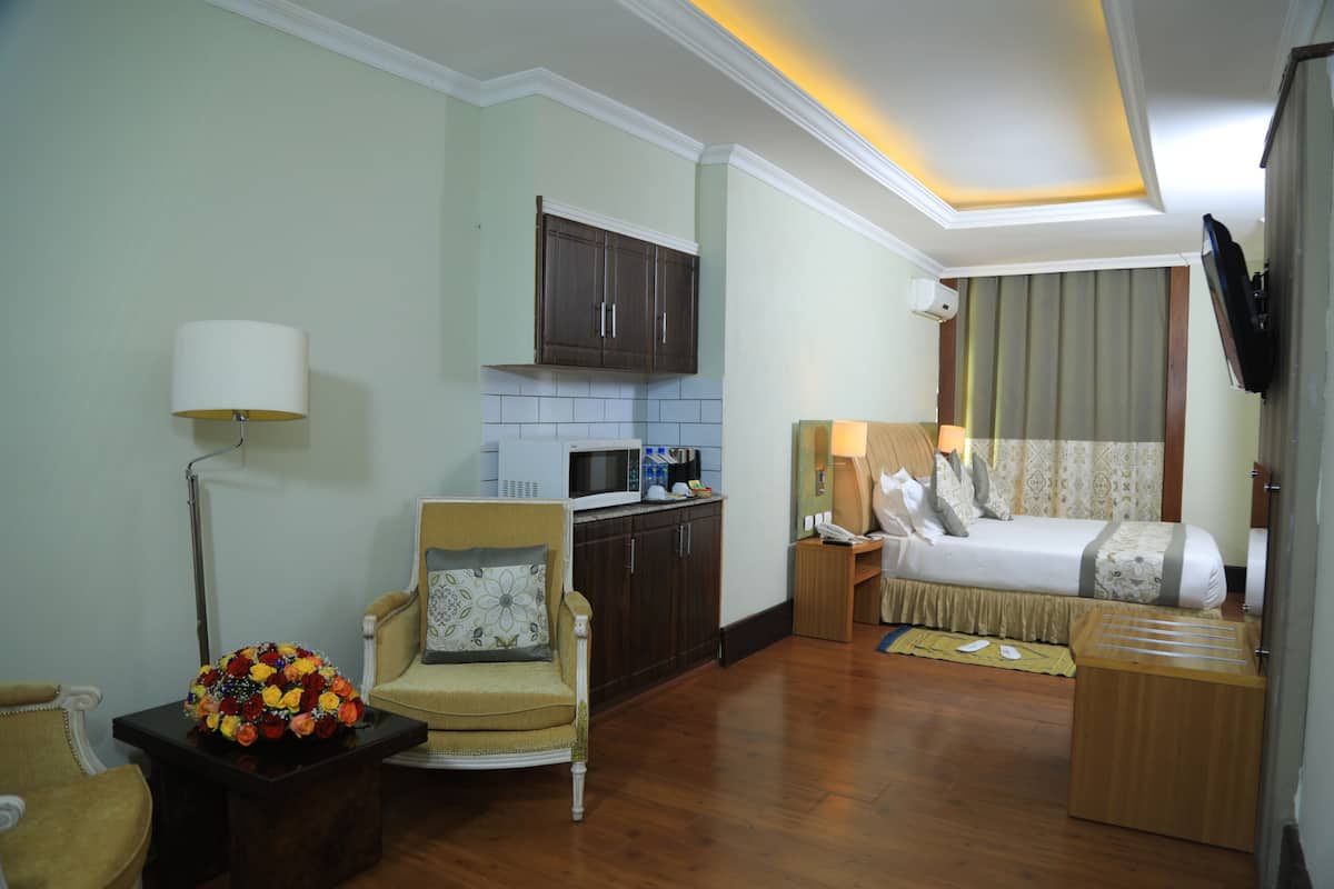 A hotel room with a bed, a chair, a small table with a flower arrangement, a microwave, and a television.