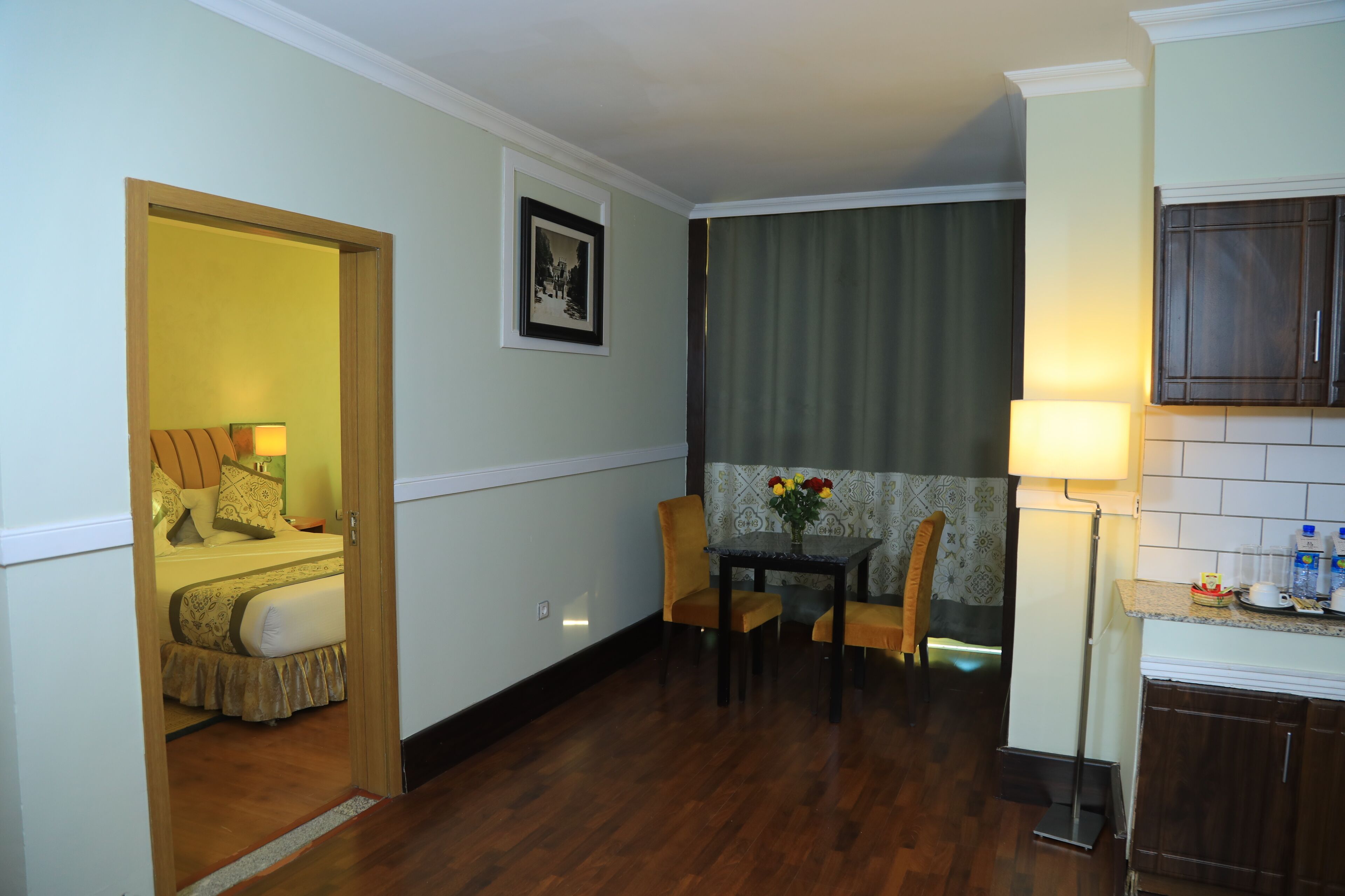Habitación de hotel con cama, una mesa de comedor con sillas, una pequeña cocina y un baño visible a través de una puerta abierta.