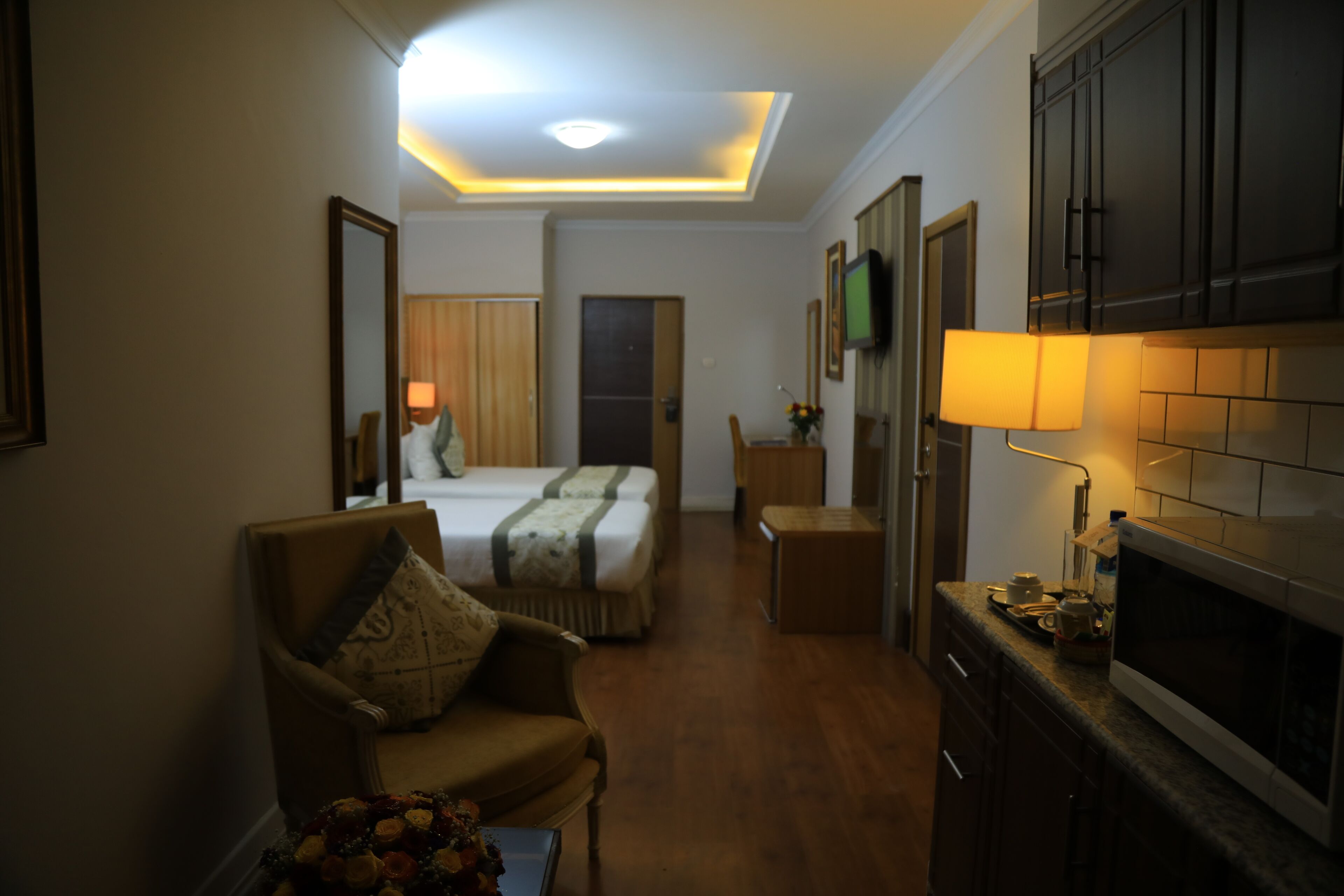A hotel room with a bed, a chair, a small table, a TV, and a kitchen area with a microwave.