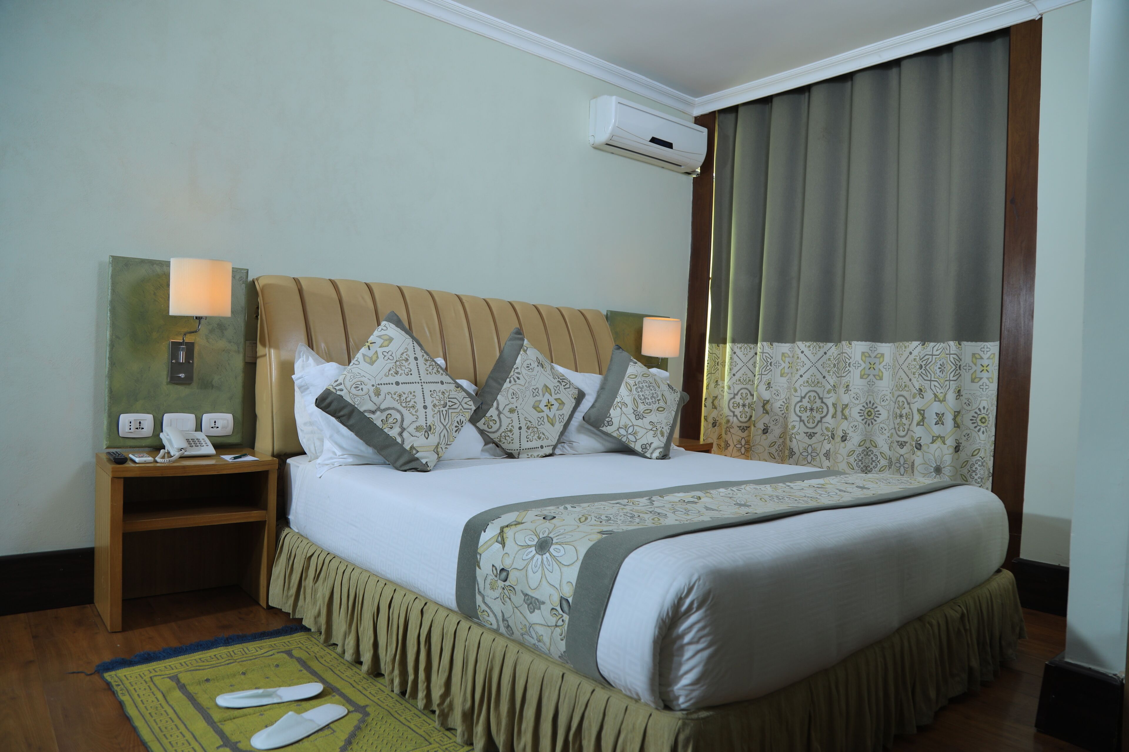 Ein Hotelzimmer mit einem großen Bett, einem Nachttisch mit Lampe, einem Telefon und einer Klimaanlage.