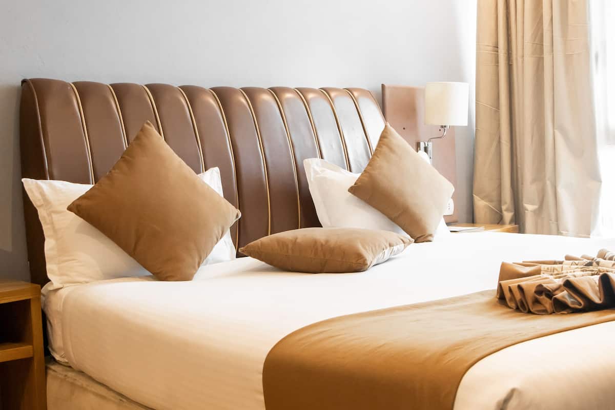 A neatly made bed with a brown headboard, white pillows, and a beige blanket.