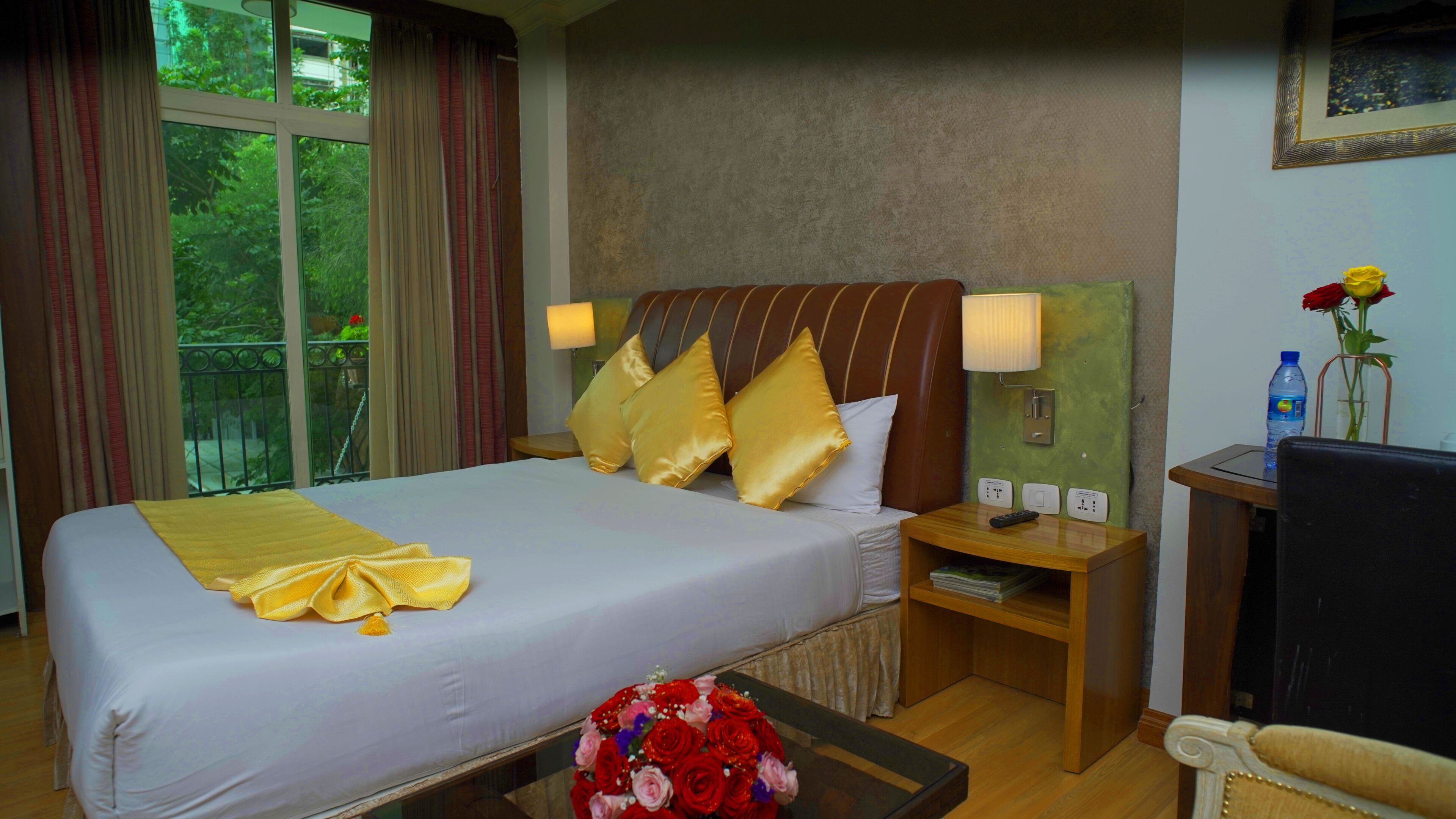 Ein Hotelzimmer mit einem großen Bett, zwei Nachttischlampen, einem Nachttisch, einem kleinen Tisch mit Blumenstrauß und einem Sessel.