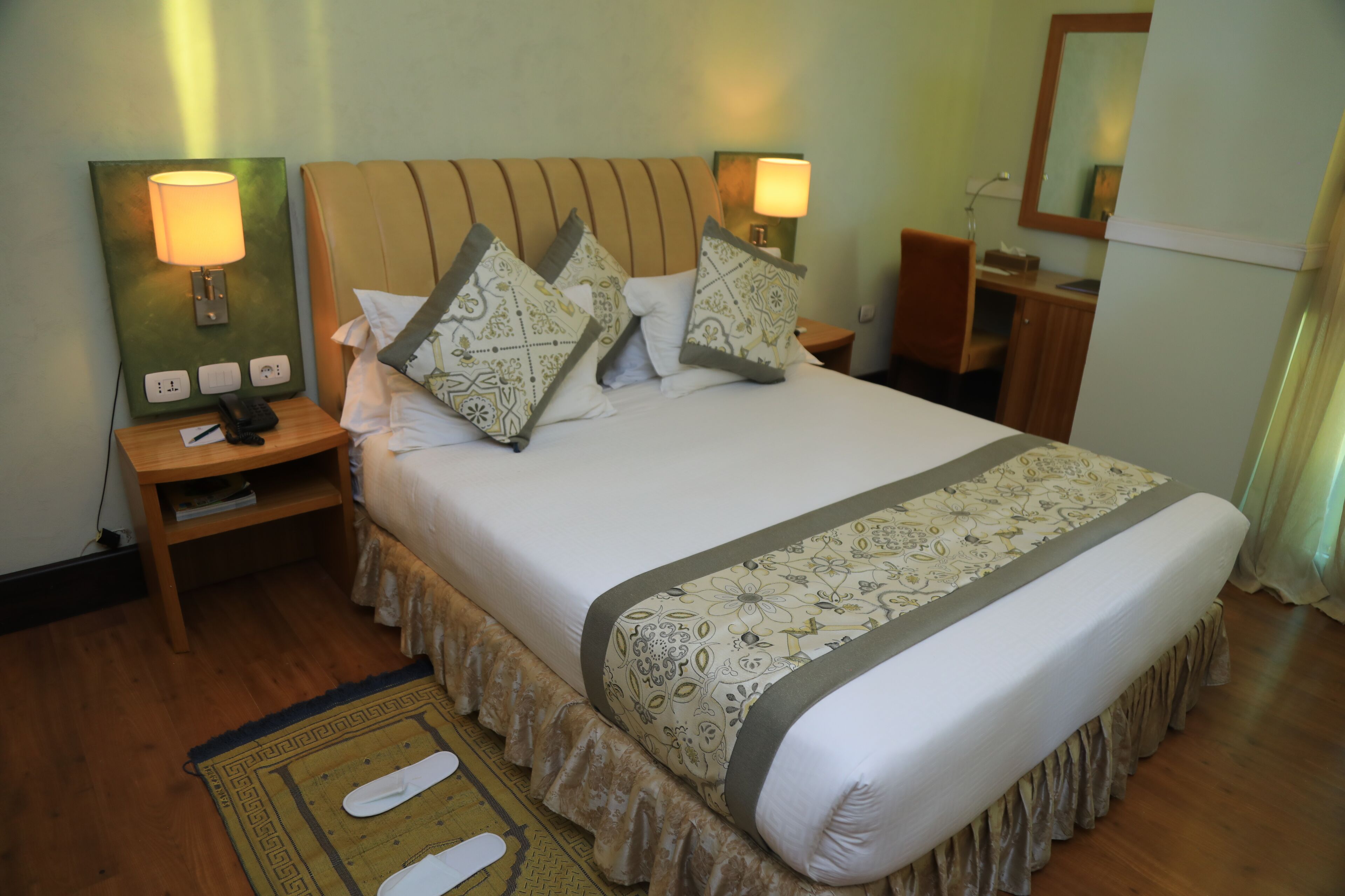 A neatly made bed with patterned pillows, a bedside lamp, and a bedside table with a phone and a book.