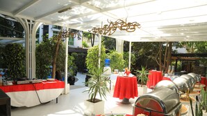 An outdoor dining area with multiple tables, some with red tablecloths, and a variety of plants. - Bonanza Addis Hotel (Addis Ababa)