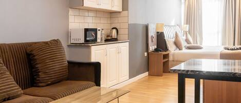 A modern hotel room with a sofa, a small table, a kitchenette, and a bed with a view of the outdoors.