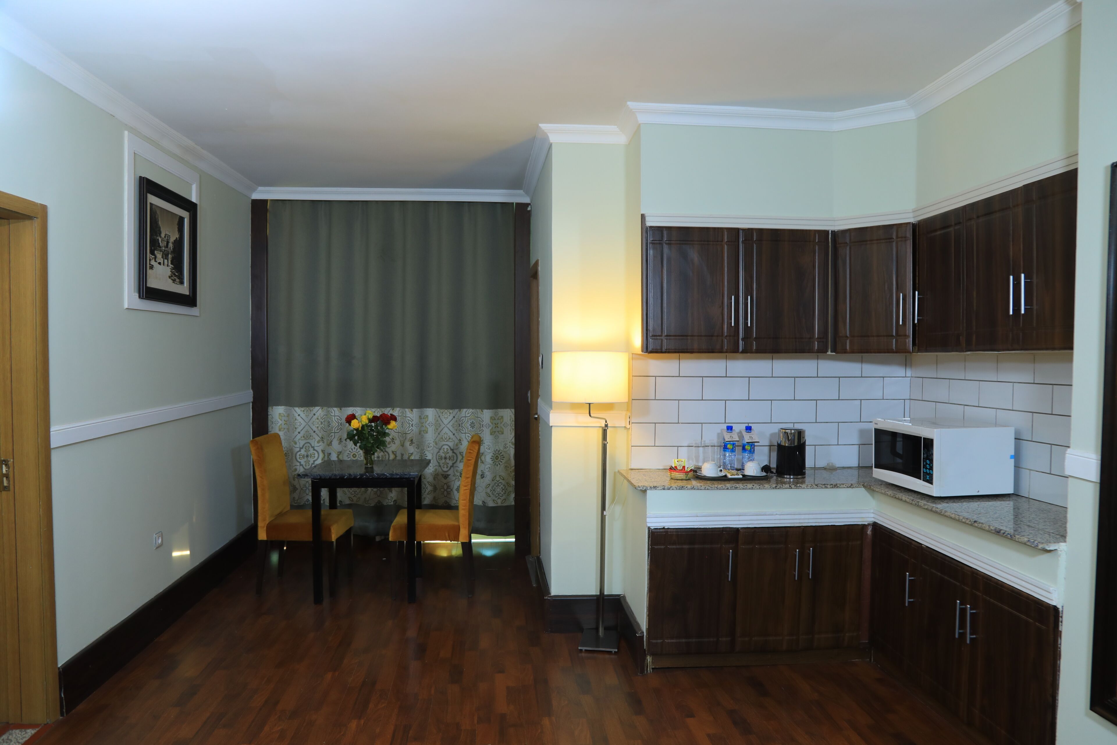 Una cocina compacta con armarios de madera oscura, un microondas blanco y una zona de comedor con mesa y sillas.