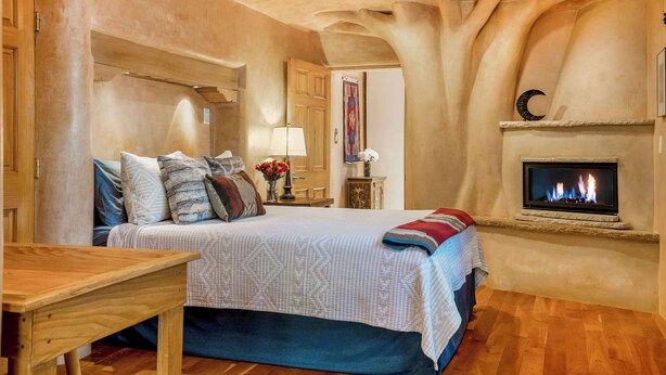 Un dormitorio con cama, una mesa de madera, una chimenea y una mesita de noche con lámpara.