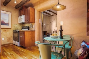 A compact kitchen with wooden cabinets, a microwave, and a stove. There is a dining area with a table and chairs, and a wine bottle on the table. - Unique Hideaway, Walk Everywhere (Santa Fe)