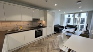 A modern kitchen with white cabinets, a herringbone wood floor, and a dining area with a white table and chairs.