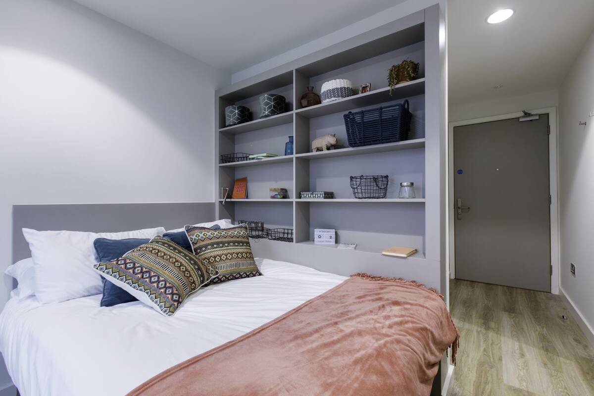 A bedroom with a bed, a shelf unit with various items, and a door.