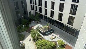 A modern building with a courtyard featuring seating areas, greenery, and a clear sky.