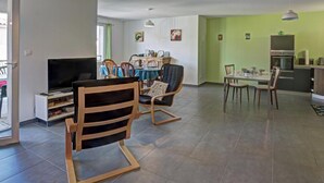 A living room with a TV, a dining area with a table and chairs, and a kitchen with a fridge and stove. - Modern Apartment with Balcony and Fiber Internet in Saint-Genest-Malifaux (Saint-Genest-Malifaux)