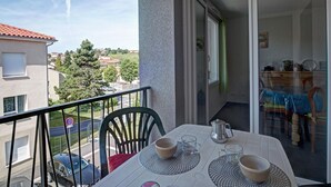 A balcony with a table set for two, chairs, a view of the street, and a glimpse of the interior. - Modern Apartment with Balcony and Fiber Internet in Saint-Genest-Malifaux (Saint-Genest-Malifaux)