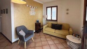 Un soggiorno con divano, poltrona, lampadario a sospensione, decorazioni a parete e una finestra.