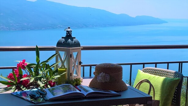 Un balcone con vista su un lago e montagne, un tavolo con un libro, una lanterna e fiori.