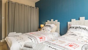 Une chambre d’hôtel avec deux lits, des rideaux gris, une tête de lit en bois et une lampe sur une table de chevet.