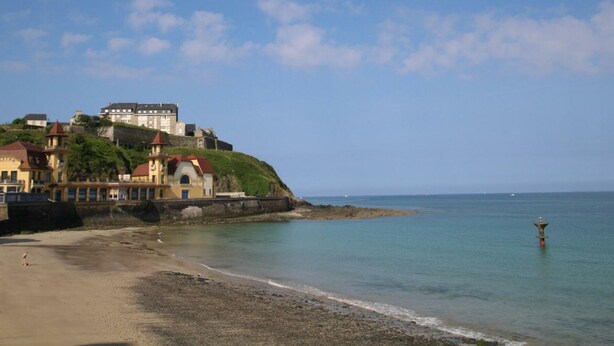 Une ville côtière qui abrite un château imposant perché sur une colline, une plage de sable et une mer calme.