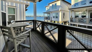 Eine Holzterrasse mit Tisch und Stühlen, mit Blick auf ein Ufer mit mehreren weißen Gebäuden.