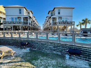 A beachfront hotel with multiple-story buildings, a swimming pool, and a wooden deck with lounge chairs.