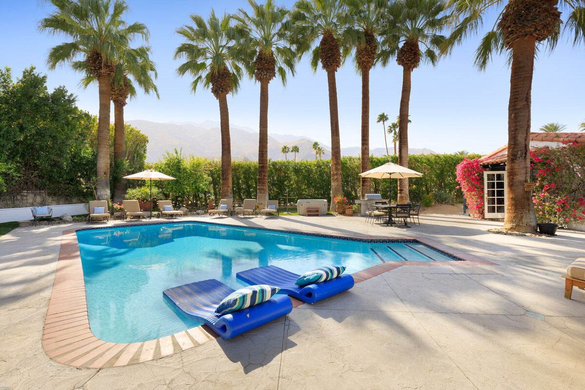 A swimming pool with lounge chairs and umbrellas, surrounded by palm trees and a view of mountains.