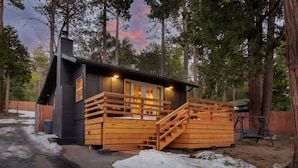 A cabin with a wooden deck, a staircase, and a swing set.
