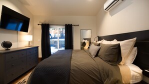A modern hotel room with a large bed, a flat-screen TV, a dresser, and an air conditioning unit.