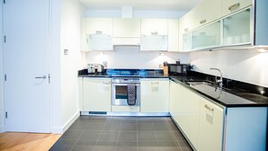 Moderni keittiö, jossa on valkoiset kaapit, musta työtaso ja ruostumattomasta teräksestä valmistetut kodinkoneet.
