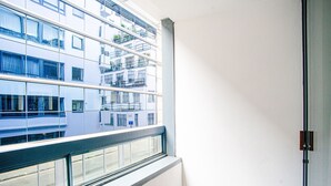 Huoneen nurkka, jossa on ikkuna, josta avautuu näkymä rakennukseen, jossa on useita parvekkeita.