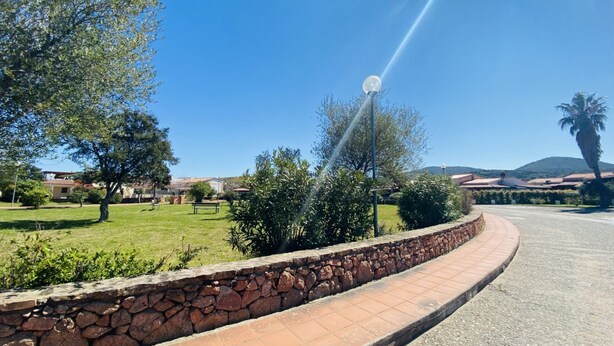 Un chemin pavé bordé d’un muret en pierre, un ciel d’un bleu limpide et un lampadaire illuminé par le soleil.