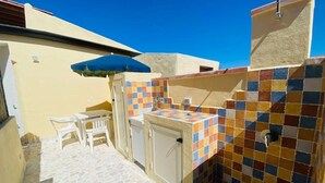 Un petit espace extérieur doté d’un sol carrelé, d’une table avec des chaises, d’un évier et d’un parasol bleu.
