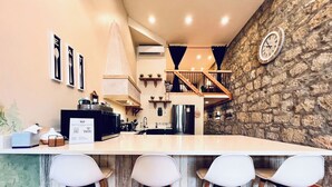 Una cucina moderna con isola centrale, sgabelli da bar, una parete a parete in pietra e una scala che conduce a un piano superiore.