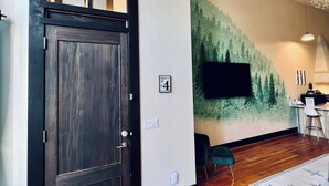 Un interno moderno con una porta in legno scuro, un tappeto d'ingresso, una TV a parete e un murale a tema foresta.